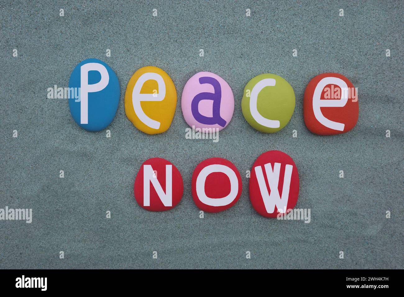 Peace Now, slogan creativo composto da lettere di pietra colorate dipinte a mano su sabbia verde Foto Stock