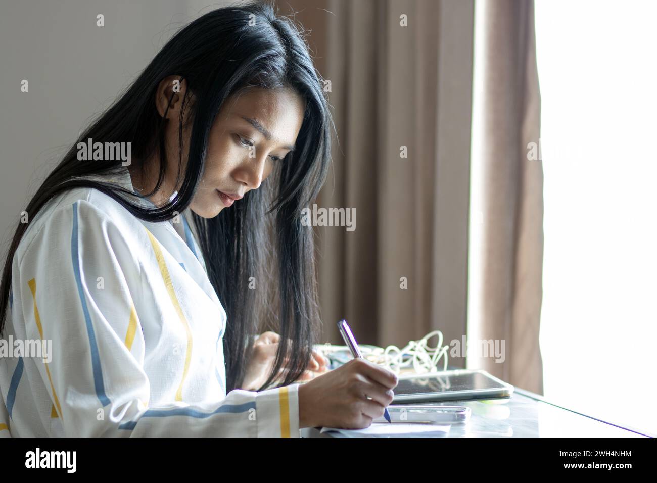 Una giovane donna lavora a un tavolo sotto una finestra Foto Stock