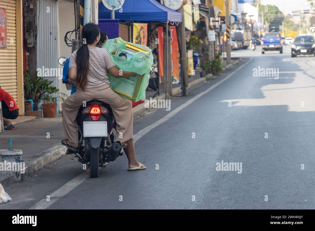 Le donne portano un dipinto avvolto su una moto, Thailandia Foto Stock