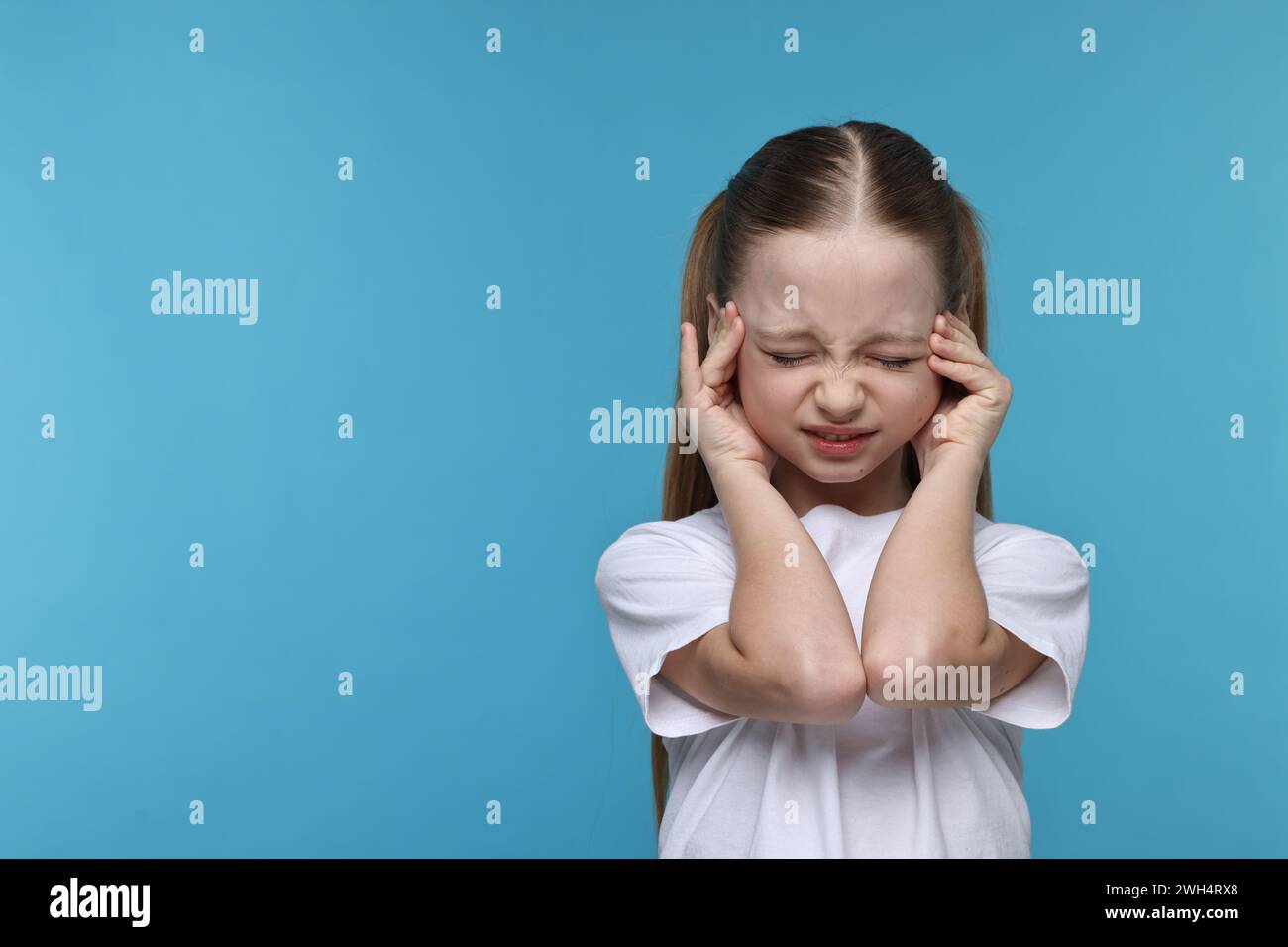 Bambina che soffre di mal di testa su sfondo azzurro. Spazio per il testo Foto Stock