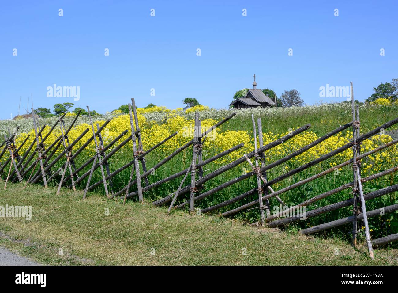 Un vecchio recinto di legno intorno ad un campo con fiori di prato e una chiesa all'orizzonte sull'isola di Kizhi in Carelia Foto Stock