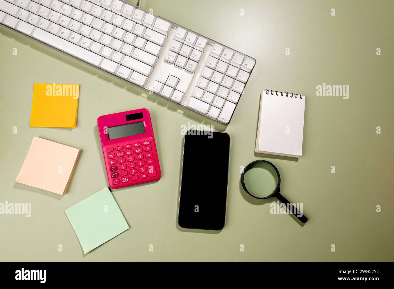 Vista ravvicinata del telefono cellulare con schermo vuoto e un quaderno vuoto e carta per appunti con lente d'ingrandimento e calcolatrice su sfondo colorato. Blan Foto Stock