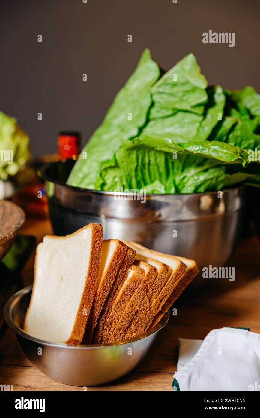 Una cucina con una ciotola di croccante lattuga romaine e un'altra con pane affettato assortito, pronta per la preparazione dei sandwich. Foto Stock