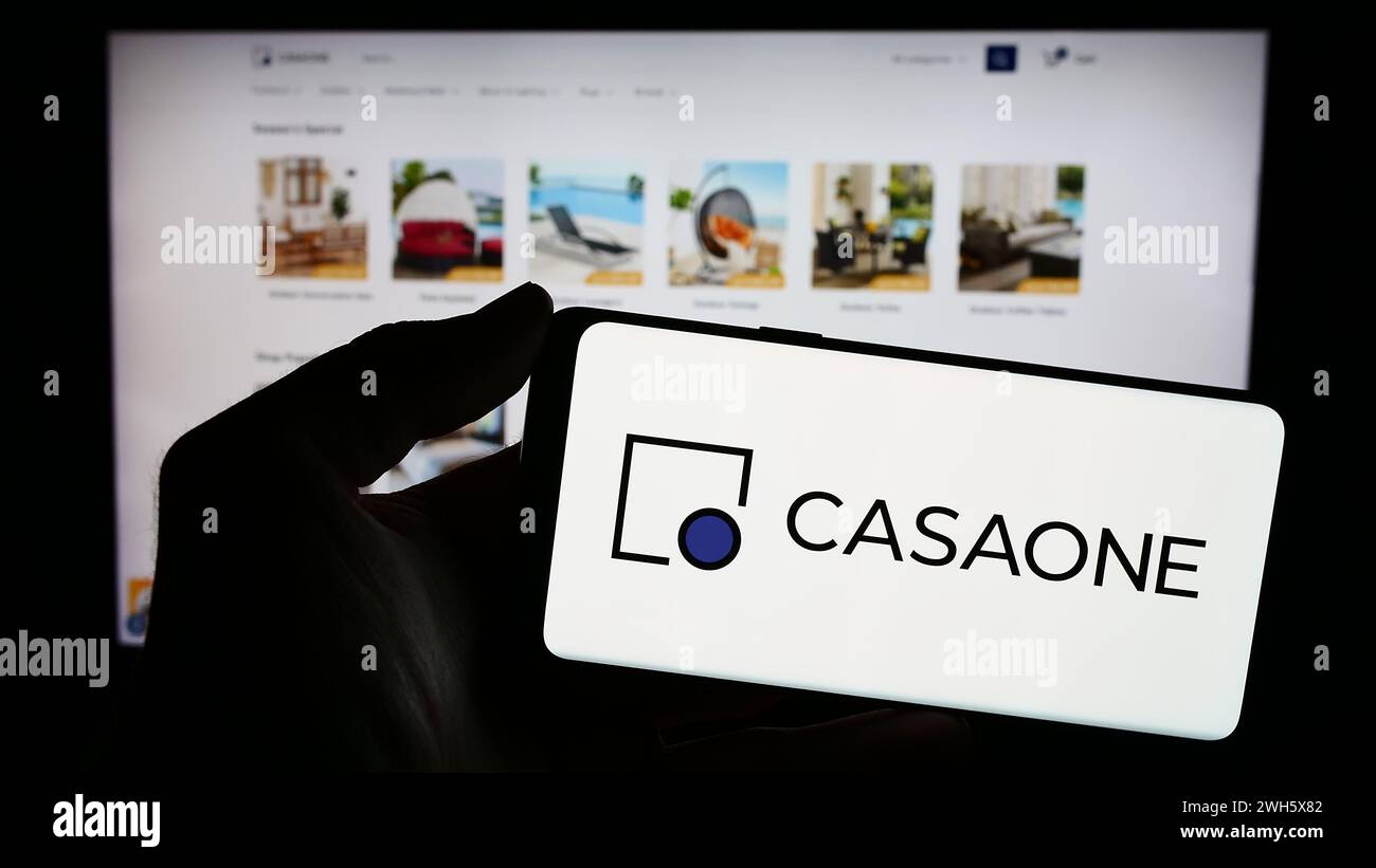 Persona che detiene un cellulare con il logo della società di e-commerce statunitense la Casa Ventures Inc (CasaOne) di fronte alla pagina Web aziendale. Mettere a fuoco il display del telefono. Foto Stock