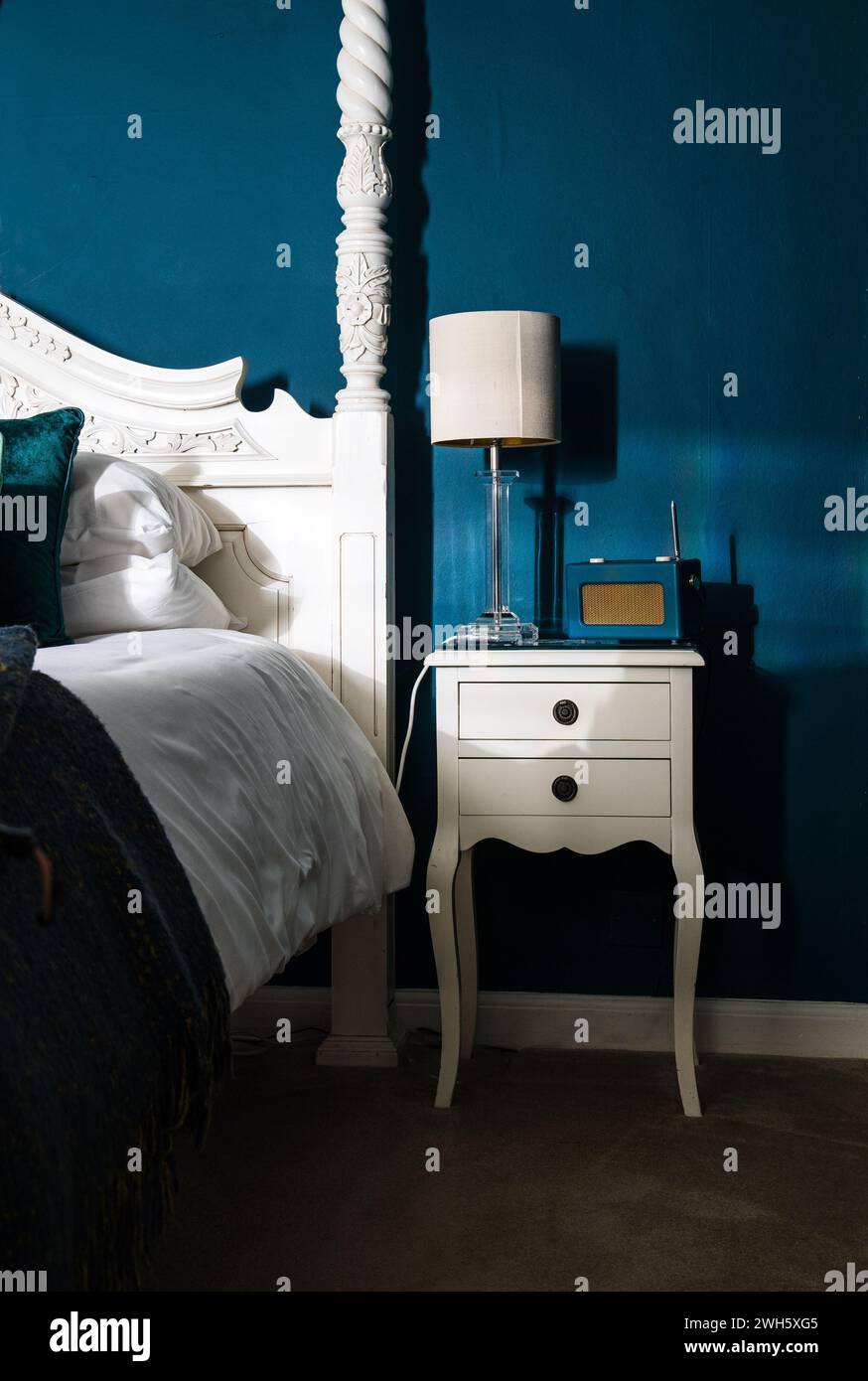 Una verticale per una camera da letto blu con elegante struttura in legno bianco e un comodino Foto Stock