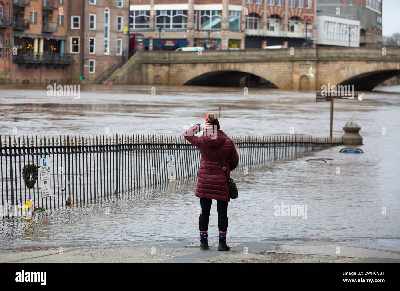 Una donna tiene il cappello per impedire che soffia a York, accanto alle rive inondate del fiume Ouse, mentre la tempesta Jocelyn colpisce e forte vento e pioggia Foto Stock