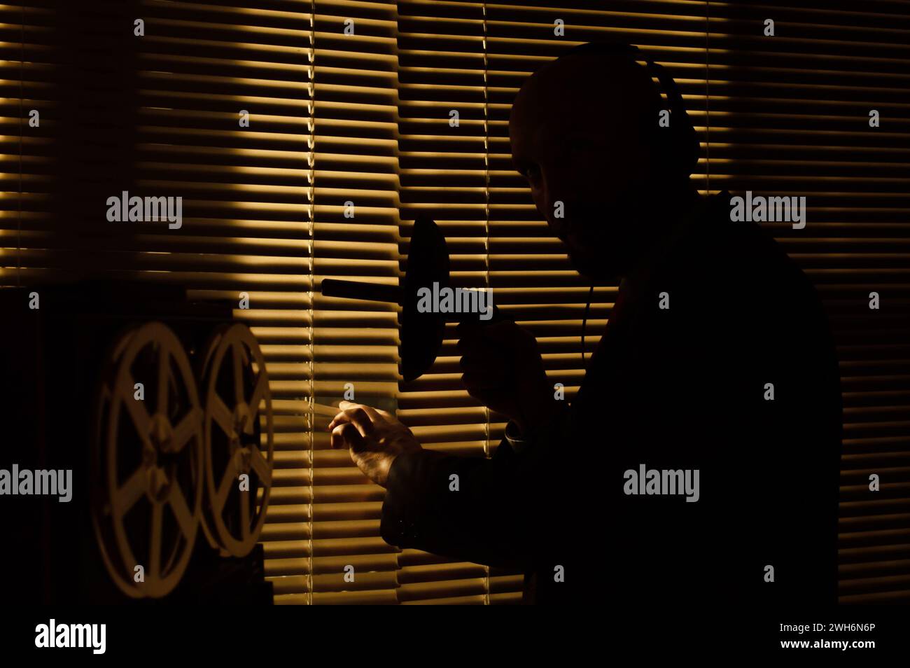 Un agente segreto dell'FBI ascolta con le cuffie e registra una conversazione sullo sfondo di una finestra con persiane, illuminazione di silhouette, selettiva Foto Stock