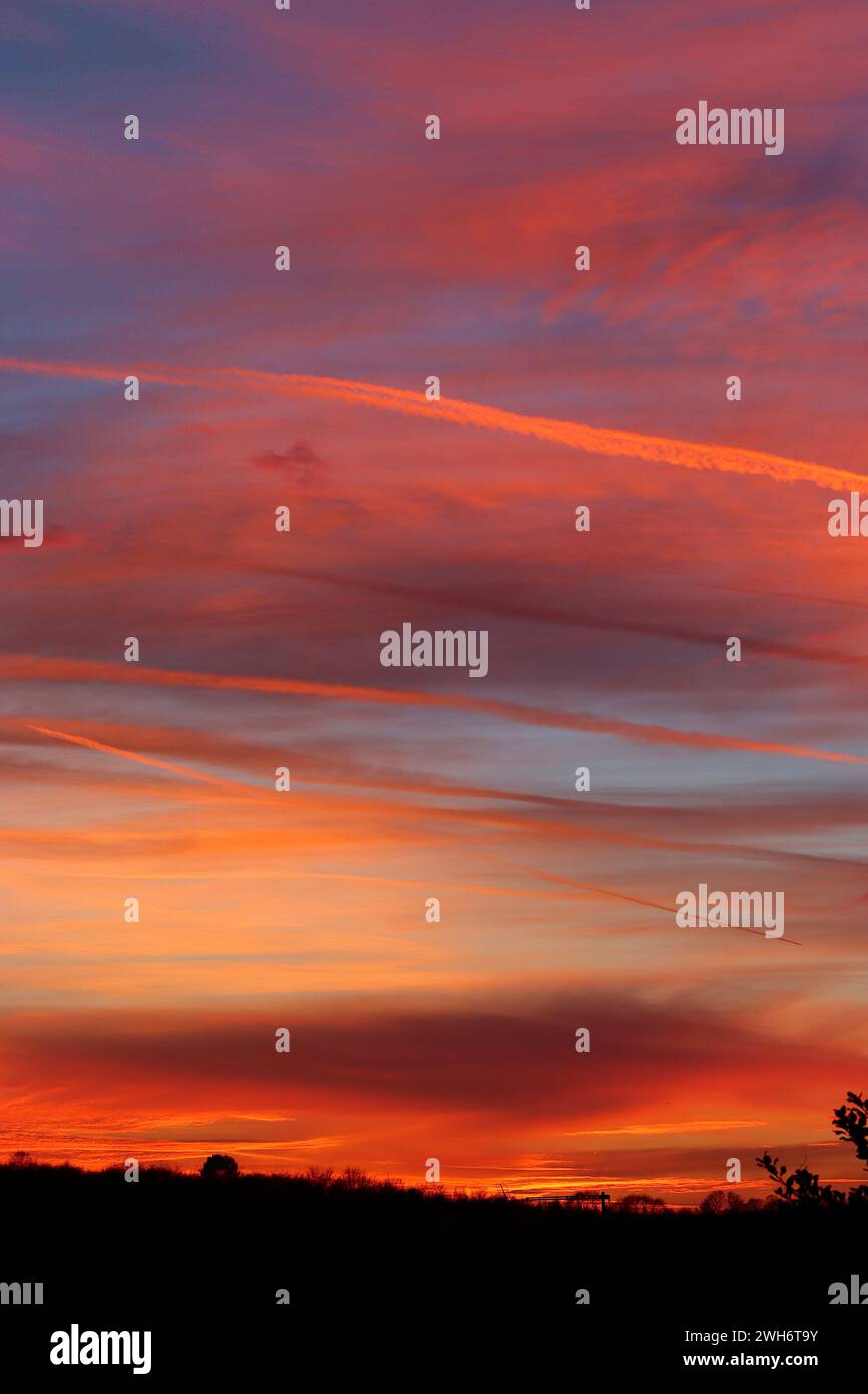 I sentieri dei vapori attraversano il cielo catturando raggi di luce serale e contrastano con le nuvole multicolore di uno spettacolare tramonto, 4 febbraio 2024. Foto Stock