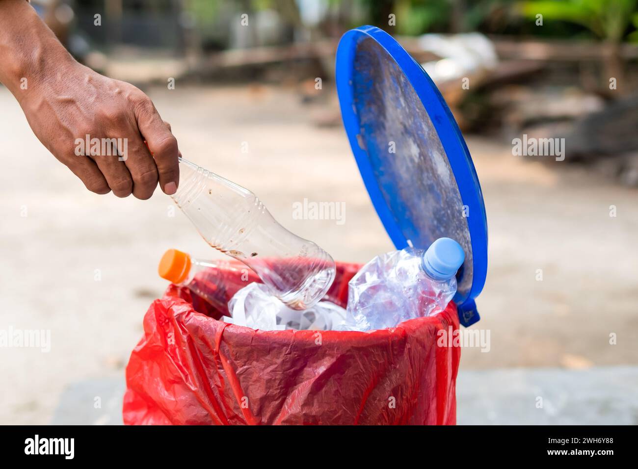 Una mano maschile che lancia una bottiglia d'acqua di plastica vuota nel cestino di riciclaggio Foto Stock