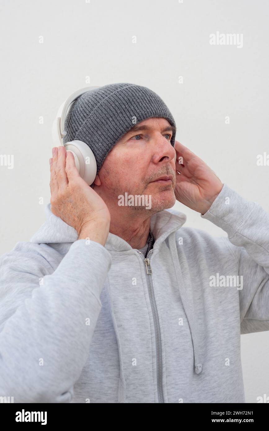 Uomo maturo che indossa un cappello in maglia e cuffie per ascoltare musica Foto Stock