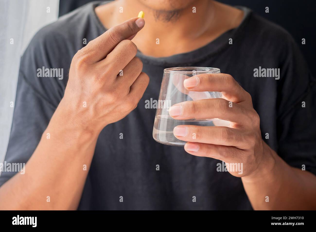 Uomo asiatico che tiene pillole e un bicchiere d'acqua Foto Stock