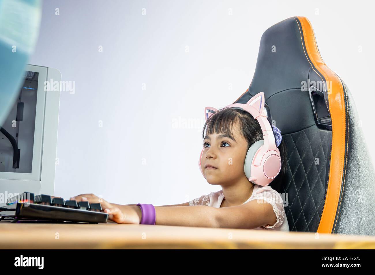 Ragazza di fronte a un computer per videogamer. Indossa cuffie rosa con orecchie di gatto. Lei fissa il monitor. Foto Stock