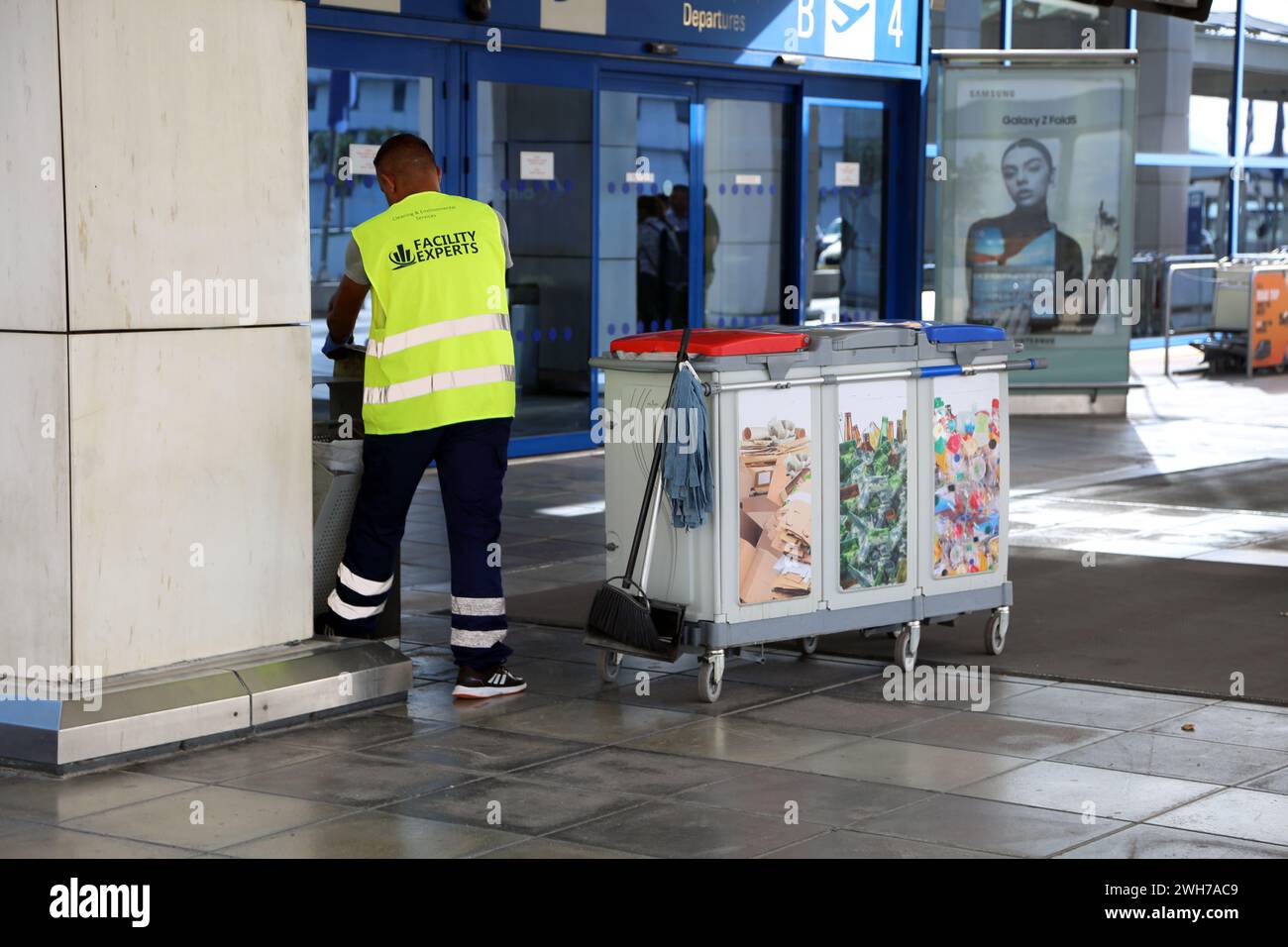 Atene Grecia Aeroporto Internazionale di Atene (AIA) Eleftherios Venizelos operaio che indossa il giubbotto ad alta visibilità che svuota i bidoni Foto Stock