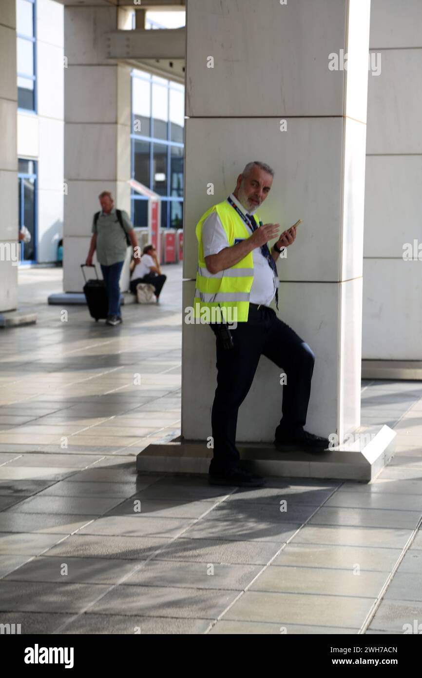 Atene Grecia Aeroporto Internazionale di Atene (AIA) Eleftherios Venizelos uomo che indossa un giubbotto ad alta visibilità tramite telefono cellulare Foto Stock