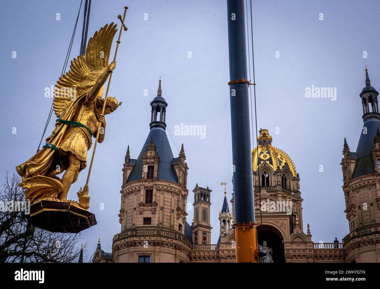 Schwerin, Germania. 8 febbraio 2024. La scultura dell'Arcangelo Michele viene rimossa dalla cupola d'oro del Castello di Schwerin per lavori di restauro utilizzando una gru mobile e caricata su un camion per il trasporto in un'officina. La figura risale al 1857 ed è ufficialmente chiamata "Arcangelo Michele che uccide il drago". L'arcangelo verrà ora pulito, restaurato e riorganizzato in un laboratorio di Berlino prima di tornare al castello in estate. L'Arcangelo Michele Slay il Drago - come è ufficialmente noto - è stato restaurato l'ultima volta 30 anni fa. Crediti: Jens Büttner/dpa/Alamy Live News Foto Stock