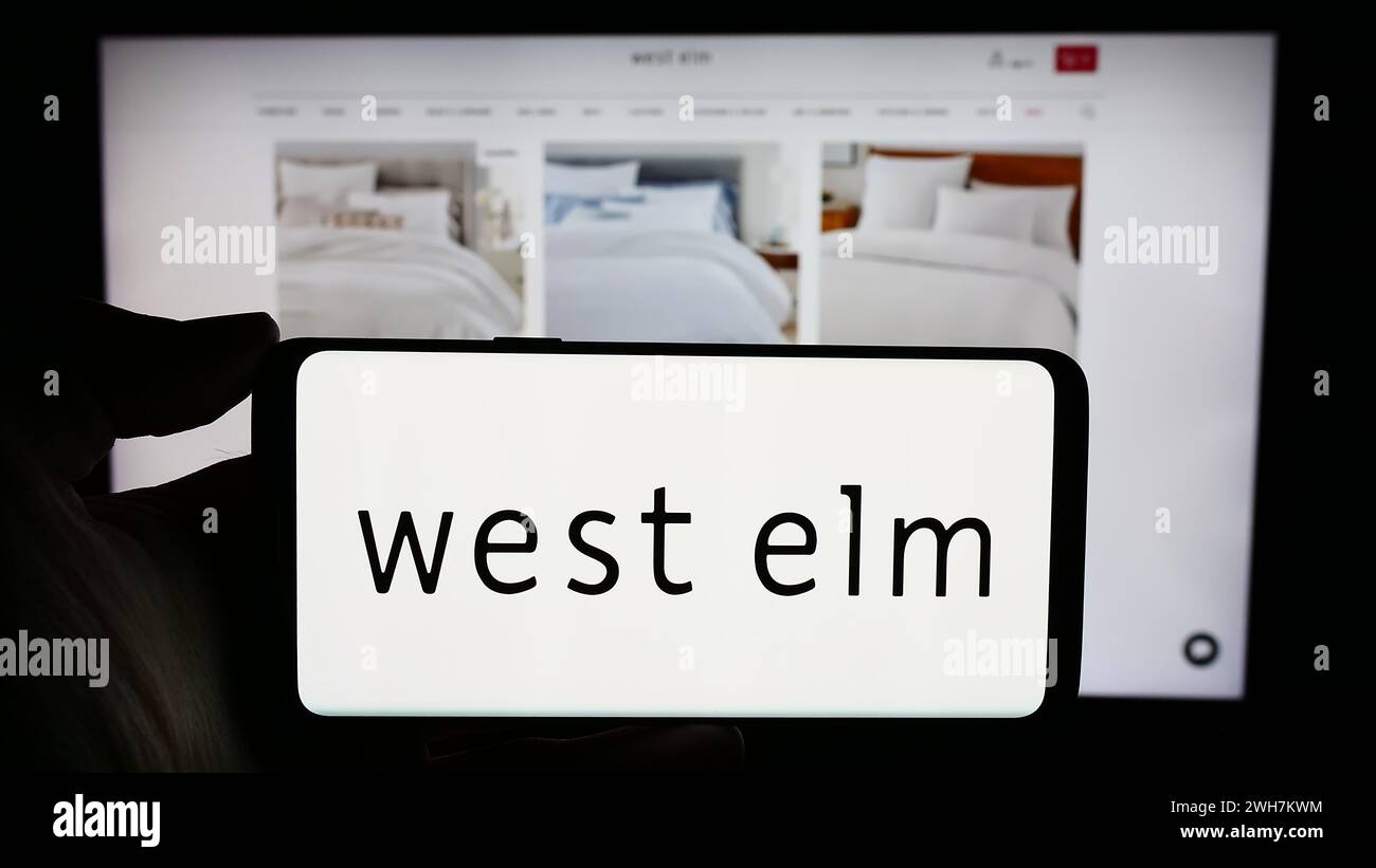 Persona che detiene un cellulare con il logo della società di arredamento West Elm di fronte alla pagina web aziendale. Mettere a fuoco il display del telefono. Foto Stock