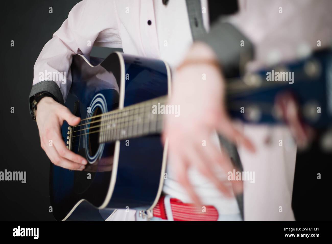 Un giovane uomo sottile e attraente in camicia bianca che suona la chitarra blu su sfondo nero, primo piano Foto Stock