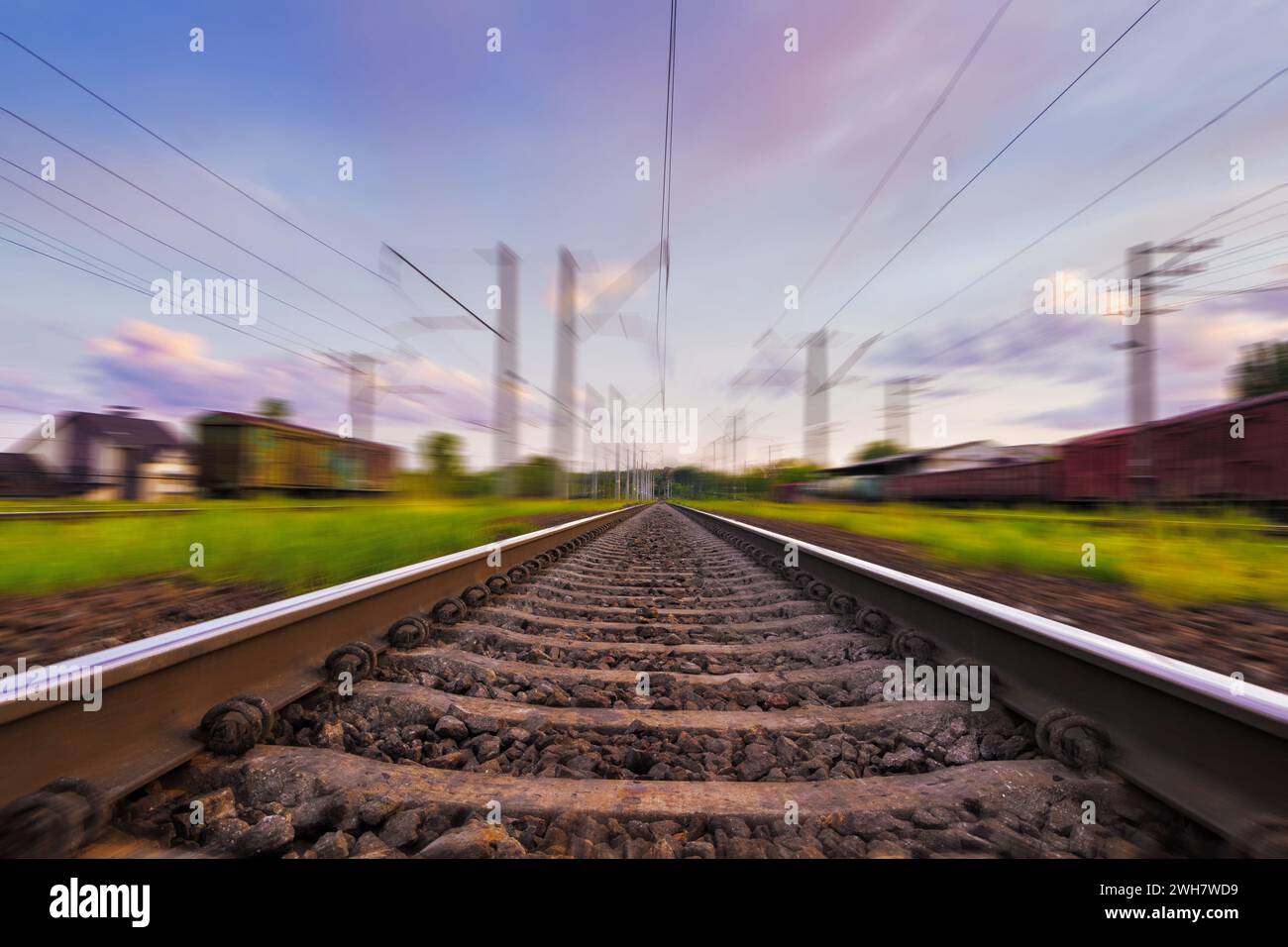 Ferrovia in movimento con effetto di sfocatura del movimento al tramonto con un cielo meraviglioso e nuvole viola. Trasporto ferroviario. Foto Stock