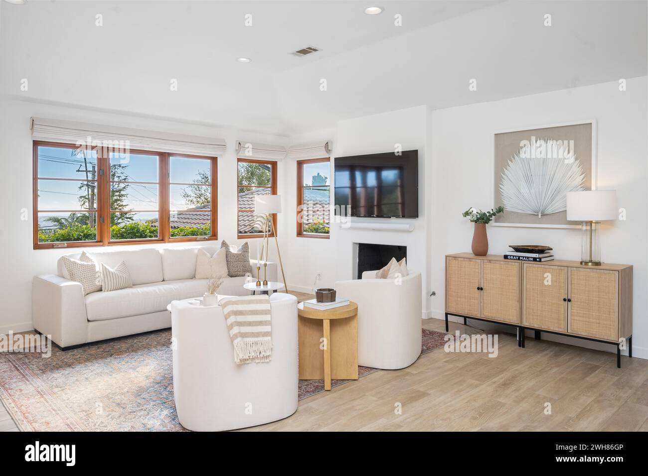 Spazioso soggiorno con pavimenti in legno duro, ampie finestre, eleganti divani bianchi e moderno tavolino da caffè Foto Stock