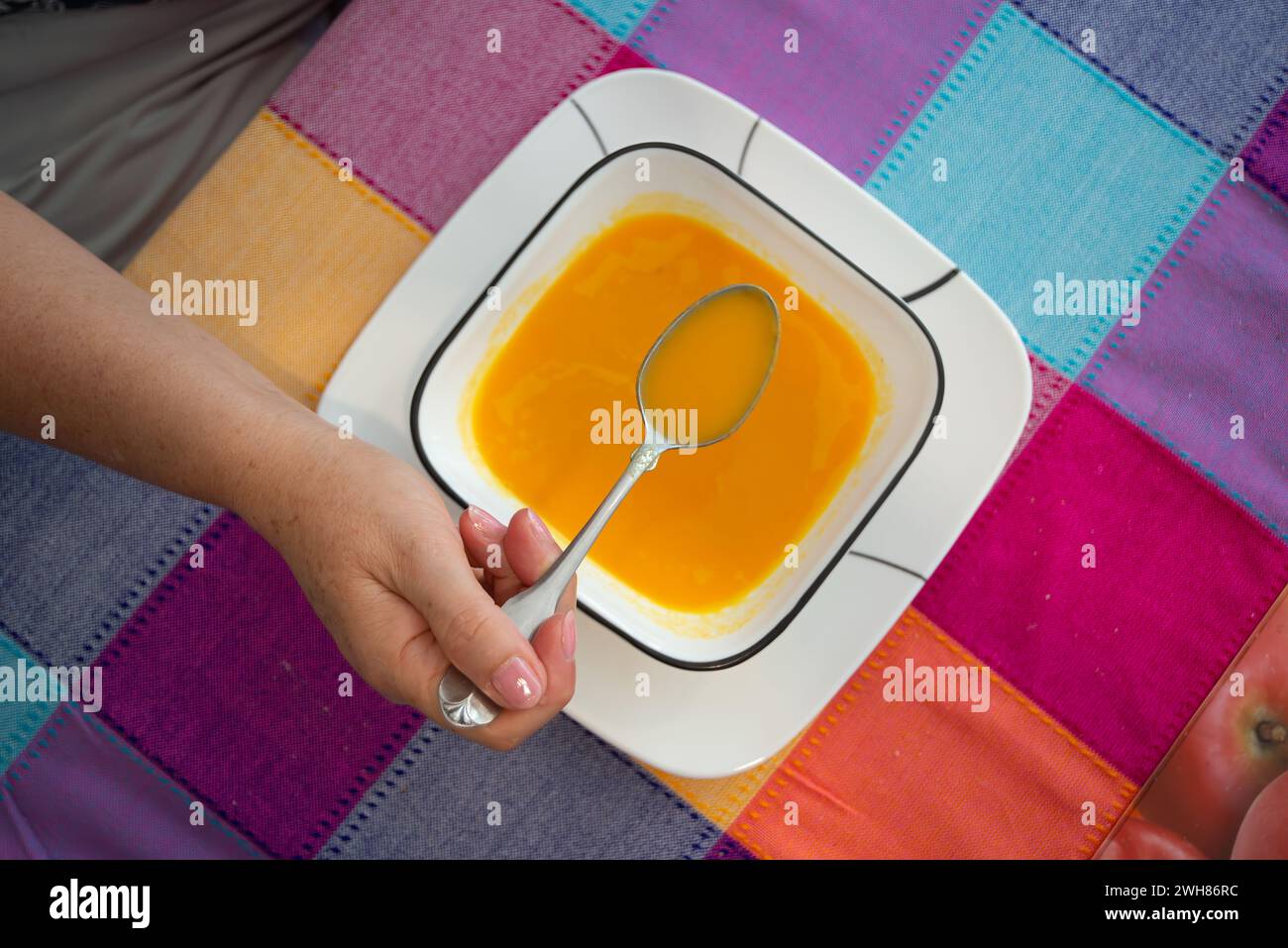Mano con cucchiaio per mangiare una zuppa di carote Foto Stock
