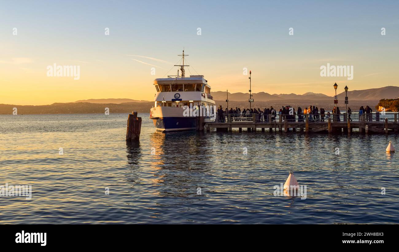 Desenzano del Garda, Italia - 4 gennaio 2024: Splendida vista su un molo mentre varie persone si imbarcano per un tour del lago al tramonto. Foto Stock