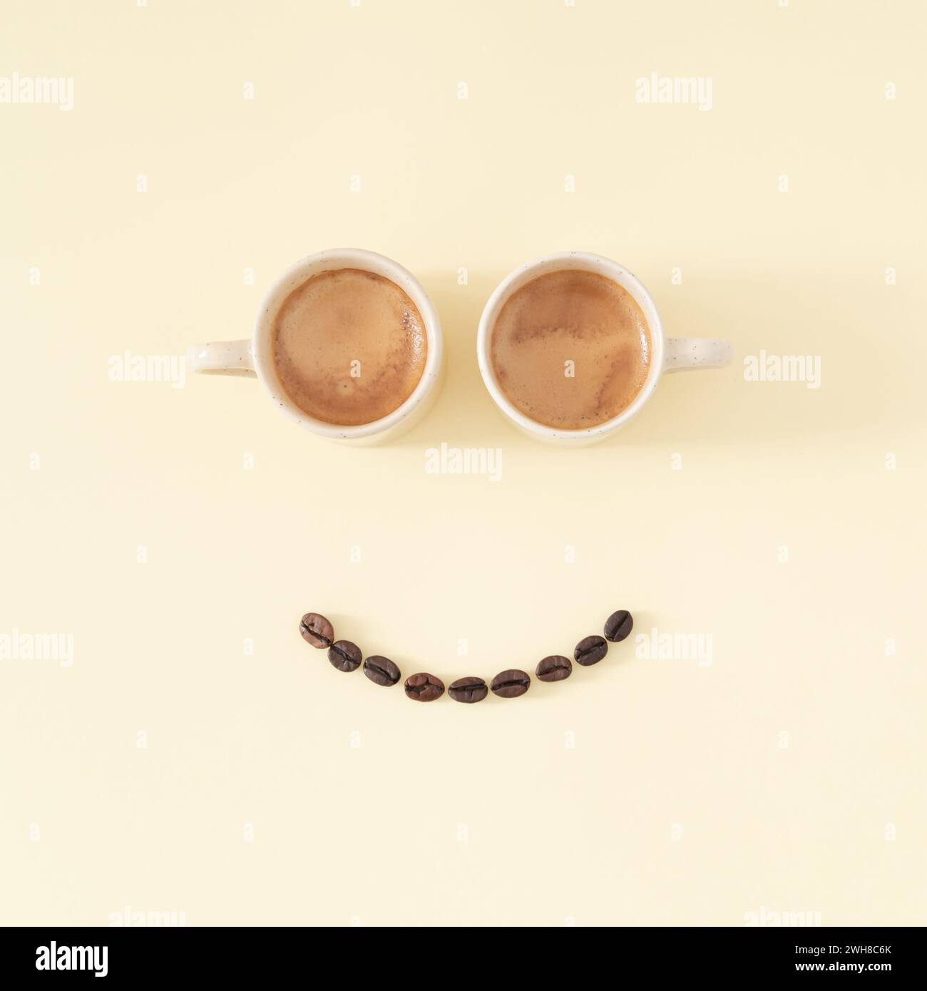 Disposizione dell'emoticon sorridente con tazze da caffè e chicchi di caffè su sfondo pastello. Concetto di caffè minimale. Pensiero creativo positivo, buon umore. Foto Stock