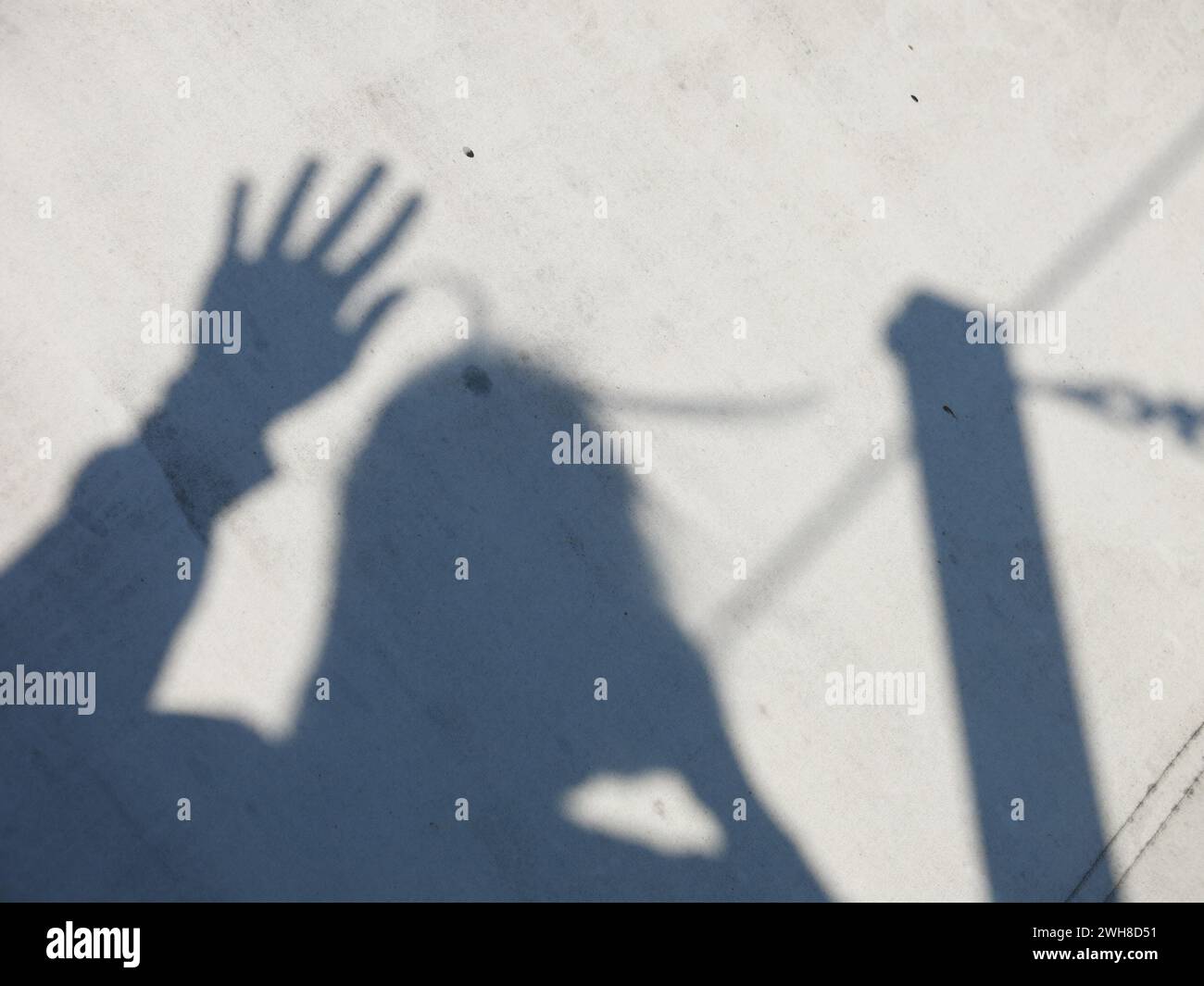 Il getto d'ombra di una donna con una mano alzata che ondeggia e i capelli che soffiano nel vento mentre si riflettono nella luce solare intensa. Foto Stock