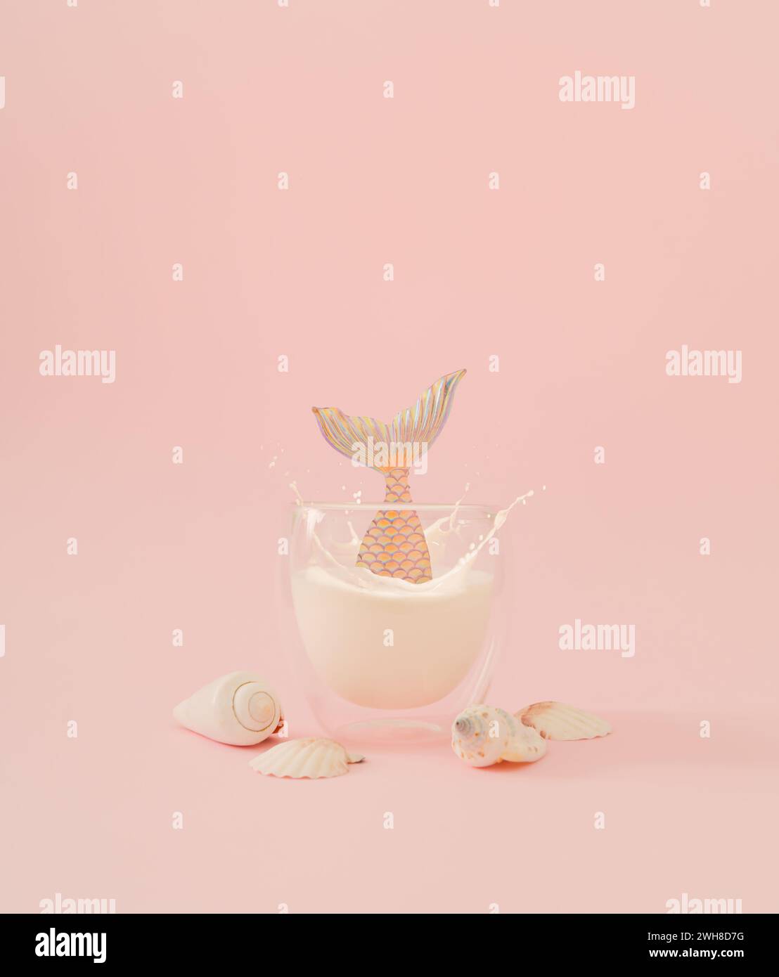 Layout creativo realizzato con sirena che si tuffa in una tazza di latte di cocco e conchiglie di mare su sfondo rosa piccante. Concetto estivo minimalista. Foto Stock