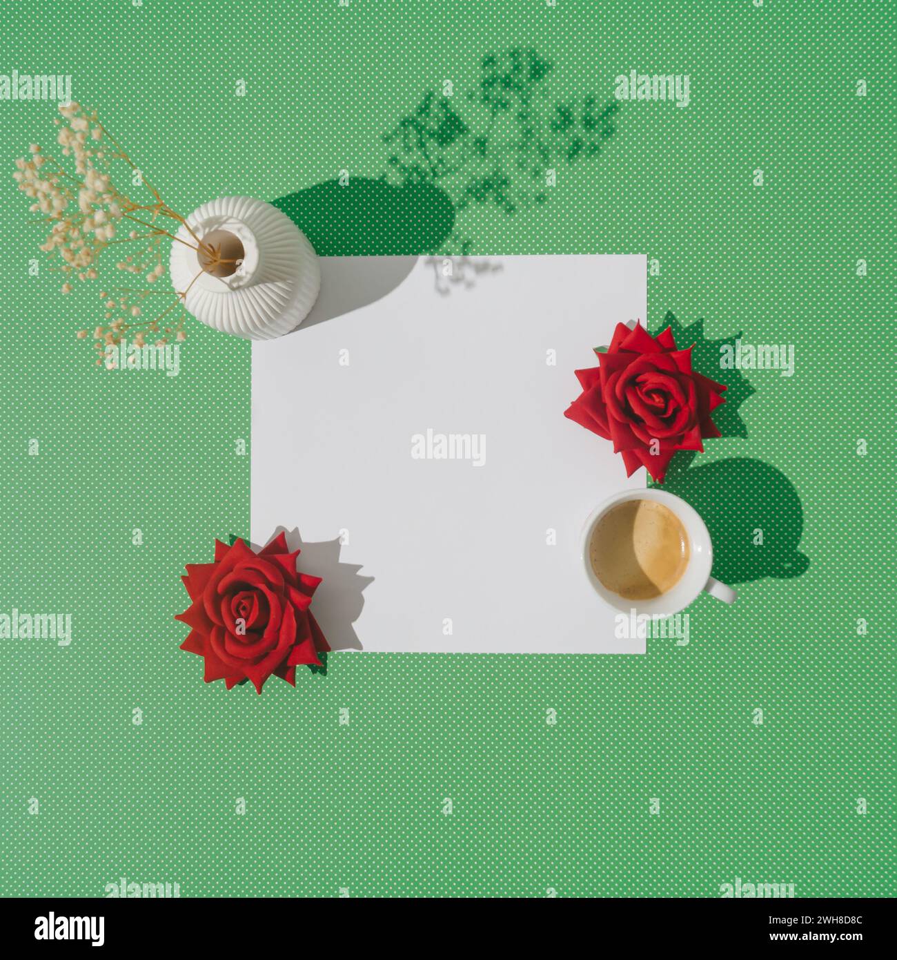 Creatività primaverile realizzata con tazza di caffè, rose rosse, vaso bianco con fiori secchi e spazio per la copia delle note su sfondo verde. Foto Stock