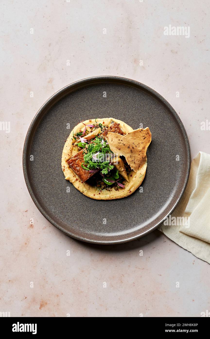 Spalla di agnello cotta a fuoco lento, purea di fava gialla, carciofo caldo, insalata di lenticchie e fagioli, erbe morbide, wafer di cumino Foto Stock