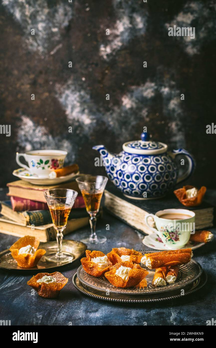 Vassoio d'argento con assortimento di biscotti Brandy Snap ripieni di panna montata e sherry in bicchieri vintage, tazze da tè e tè bianco e blu disposti Foto Stock