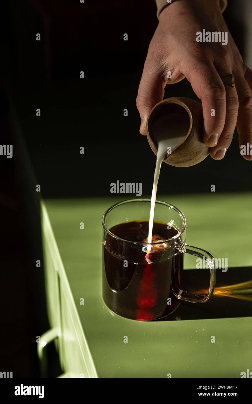 Il latte viene versato nel caffè in una tazza di vetro sul tavolo verde. Foto Stock