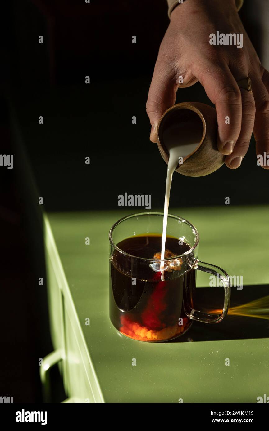 Il latte viene versato nel caffè in una tazza di vetro sul tavolo verde. Foto Stock