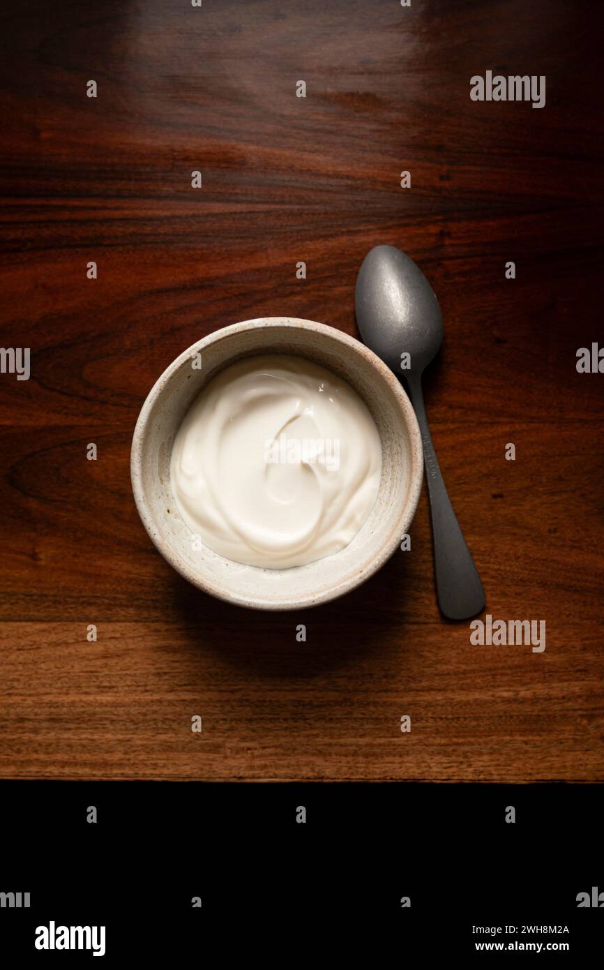 Ciotola di yogurt su un tavolo di legno antistatico con cucchiaio d'argento. Foto Stock