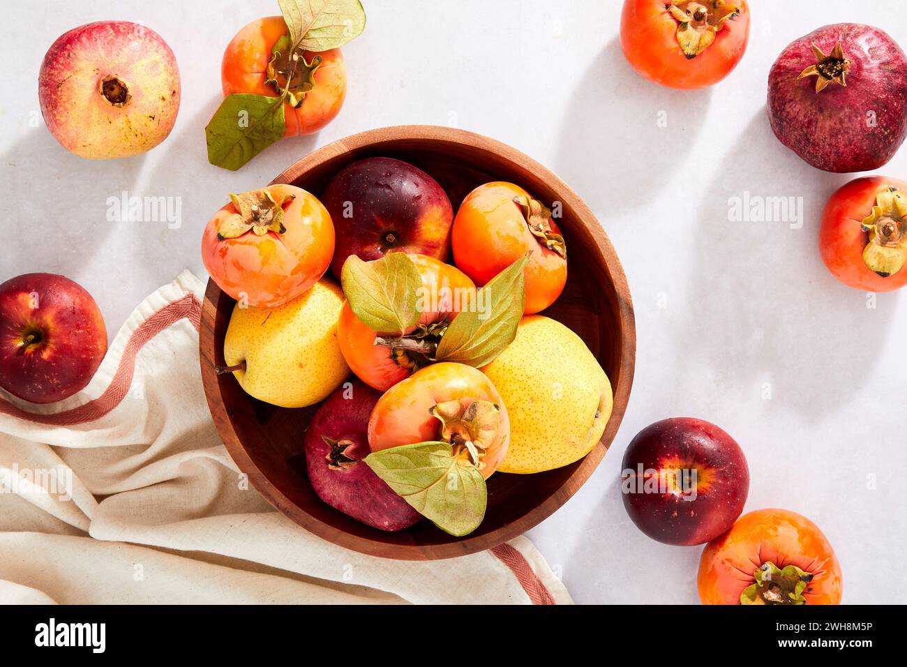 Melograni, cachi, pere e mele in un recipiente su sfondo neutro Foto Stock