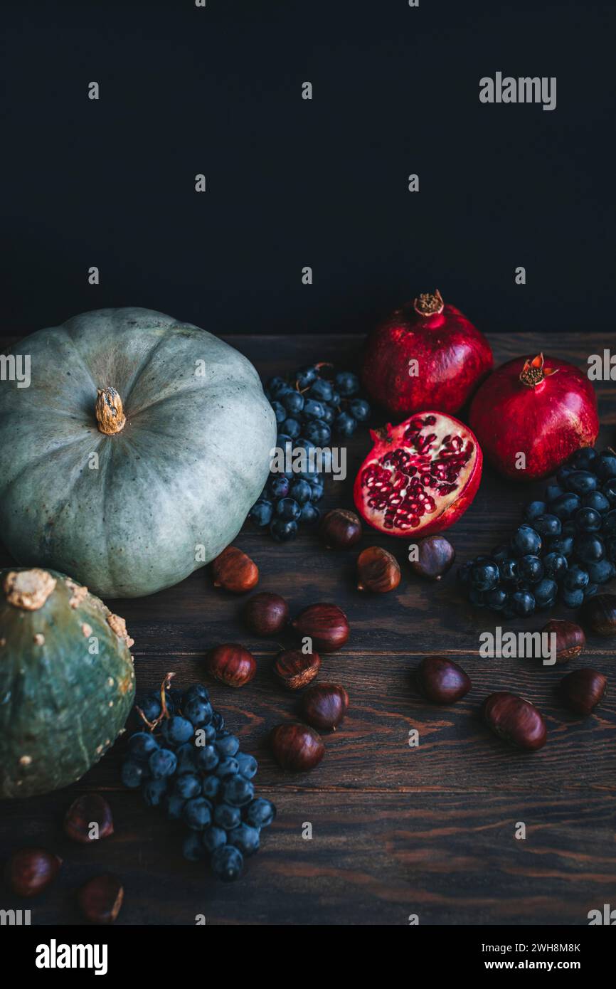 Prodotti autunnali su sfondo scuro, tra cui zucche, uva, castagne e melograno Foto Stock
