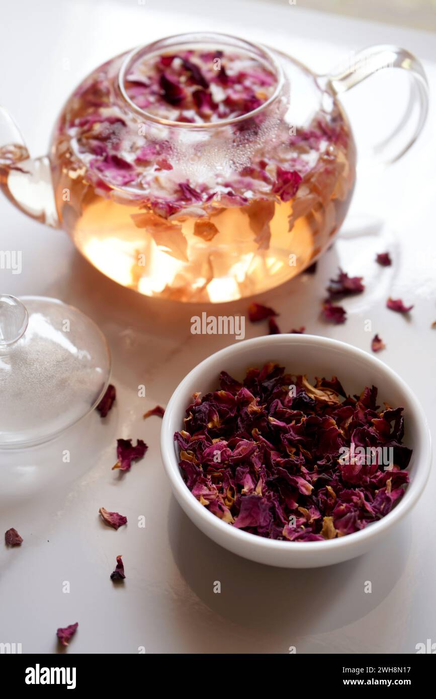 Tè alle erbe con petali di rosa con fiori secchi e teiera in primo piano. Foto Stock