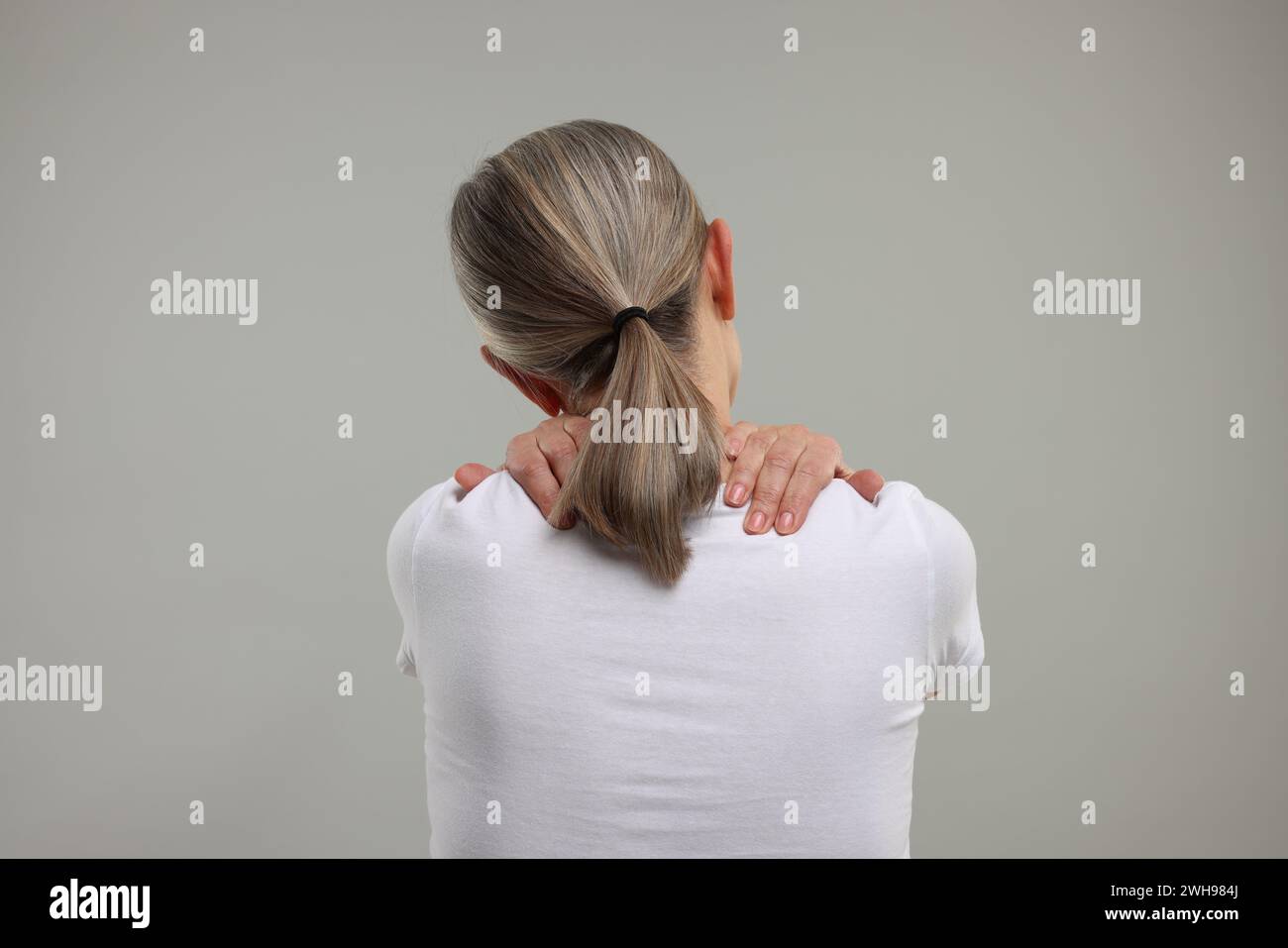 Donna matura che soffre di dolore al collo su sfondo grigio, vista posteriore Foto Stock