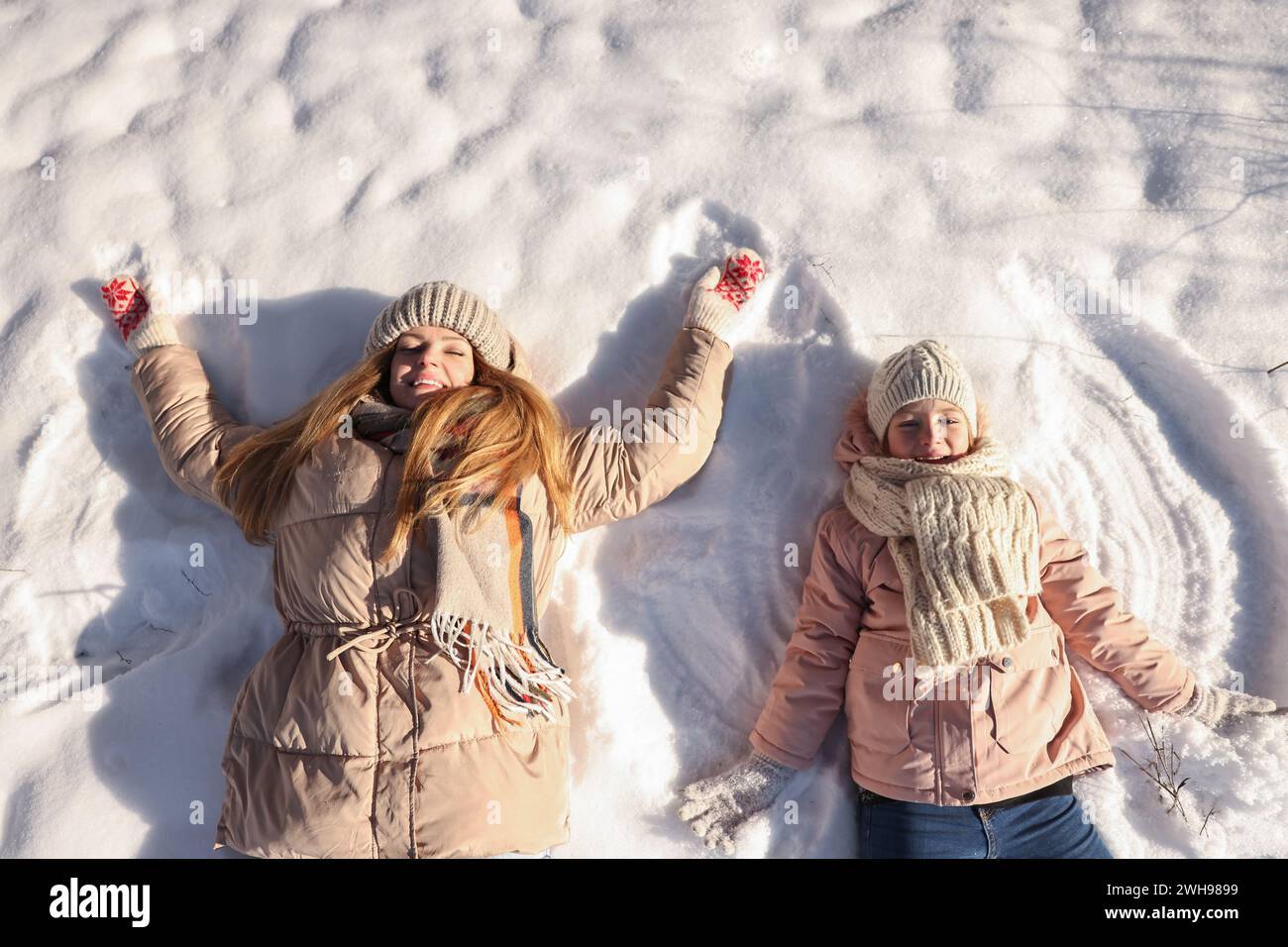 Tempo in famiglia. La madre felice e sua figlia fanno angeli di neve nelle soleggiate giornate invernali, sopra la vista Foto Stock