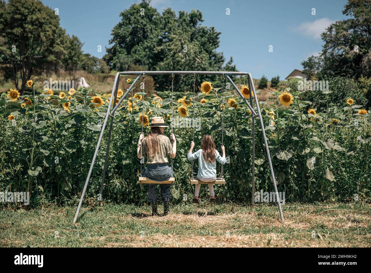 Immagine stravagante di due sorelle su un'altalena che si godono l'estate in un campo di magici girasoli Foto Stock