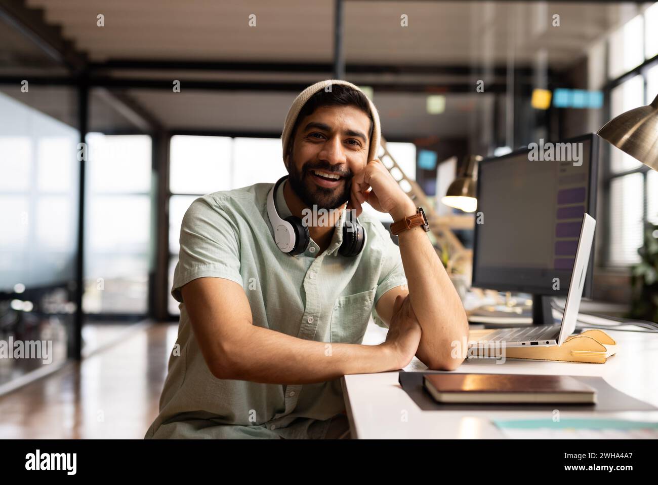Il giovane asiatico sorride alla sua scrivania in ufficio, vestito per affari informali Foto Stock