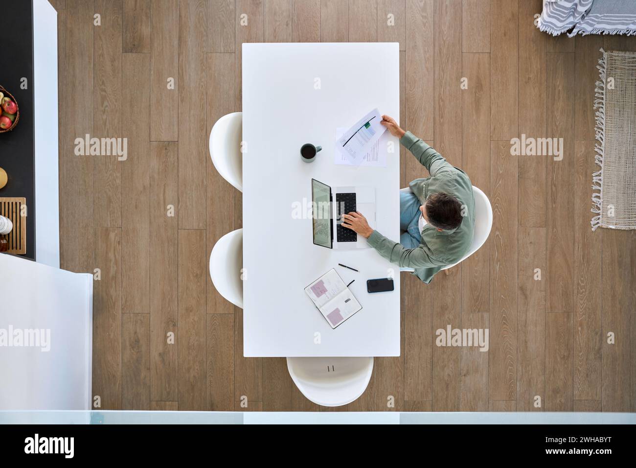 Uomo maturo che lavora su un computer portatile seduto al tavolo della cucina di casa, vista dall'alto. Foto Stock