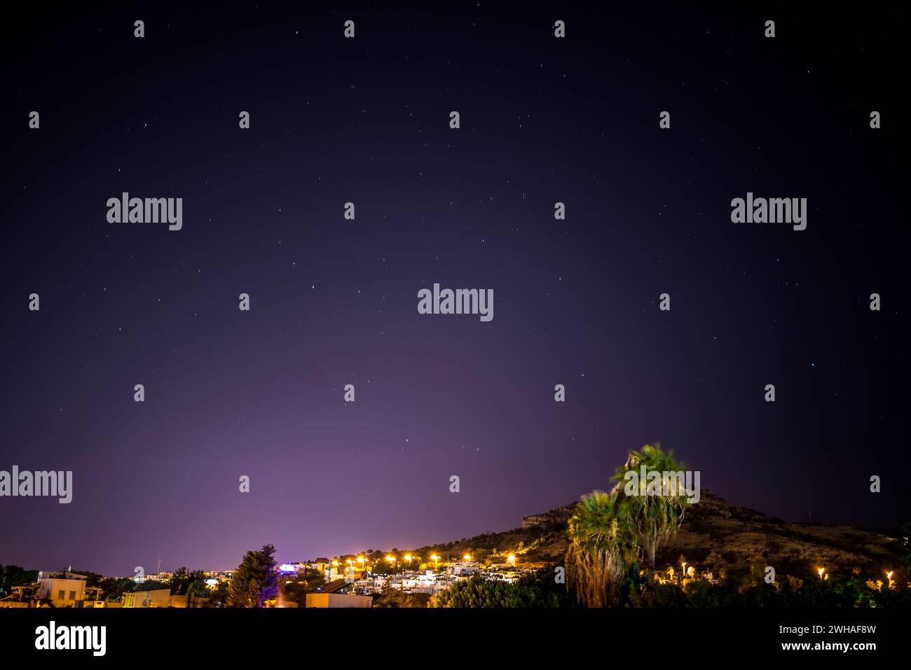 Un'affascinante miscela di montagne e città sotto un cielo stellato, dove le luci celesti incontrano il bagliore dei paesaggi urbani. Foto Stock