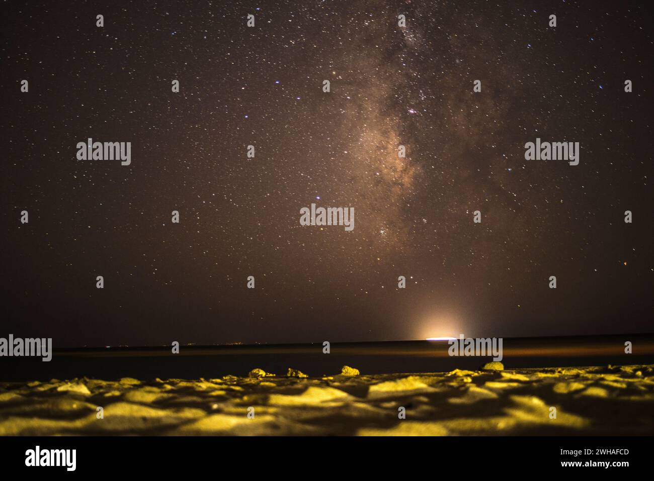 Una scena costiera mozzafiato mentre la via Lattea adorna il cielo notturno sul mare e sulla montagna, creando una meraviglia serena e cosmica. Foto Stock