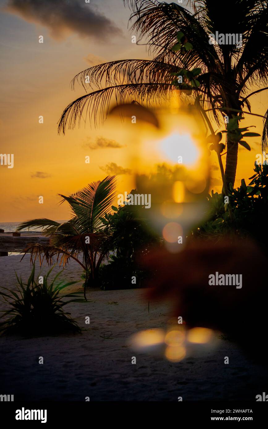 Un momento accattivante sorseggiando un bicchiere da cocktail al tramonto delle Maldive, mescolando sapori esotici con la tranquilla bellezza del paradiso costiero. Foto Stock