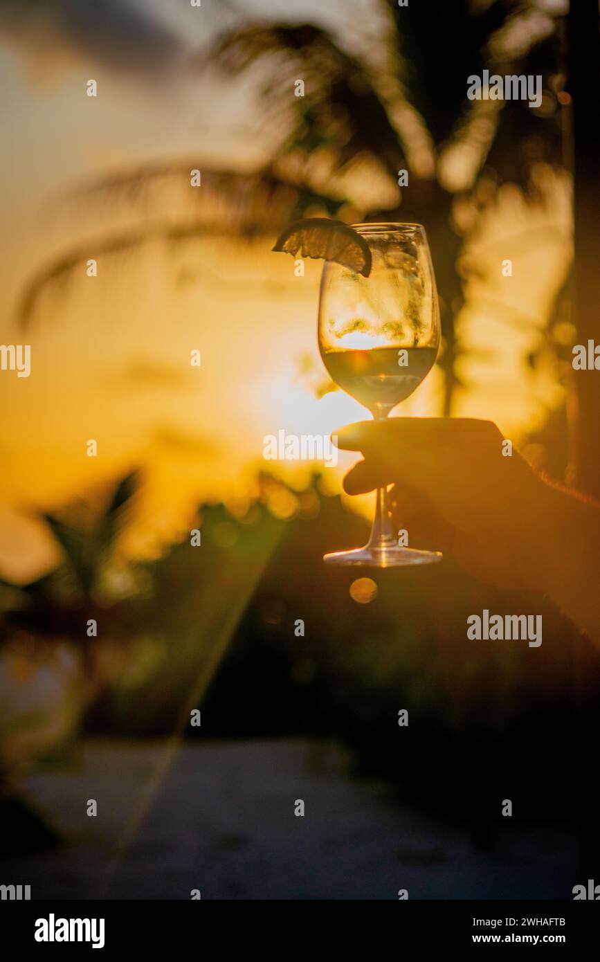 Un momento accattivante sorseggiando un bicchiere da cocktail al tramonto delle Maldive, mescolando sapori esotici con la tranquilla bellezza del paradiso costiero. Foto Stock