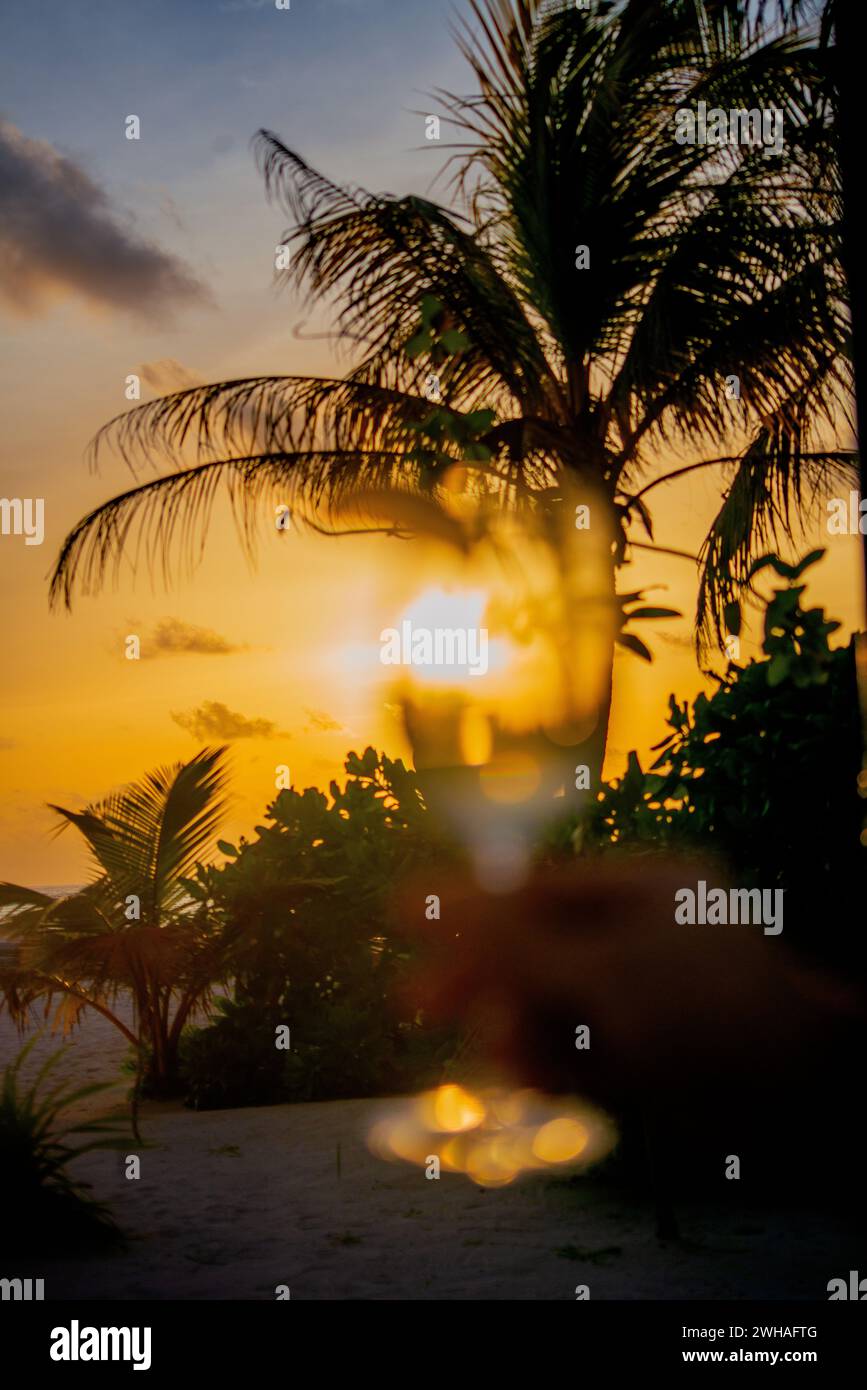 Un momento accattivante sorseggiando un bicchiere da cocktail al tramonto delle Maldive, mescolando sapori esotici con la tranquilla bellezza del paradiso costiero. Foto Stock