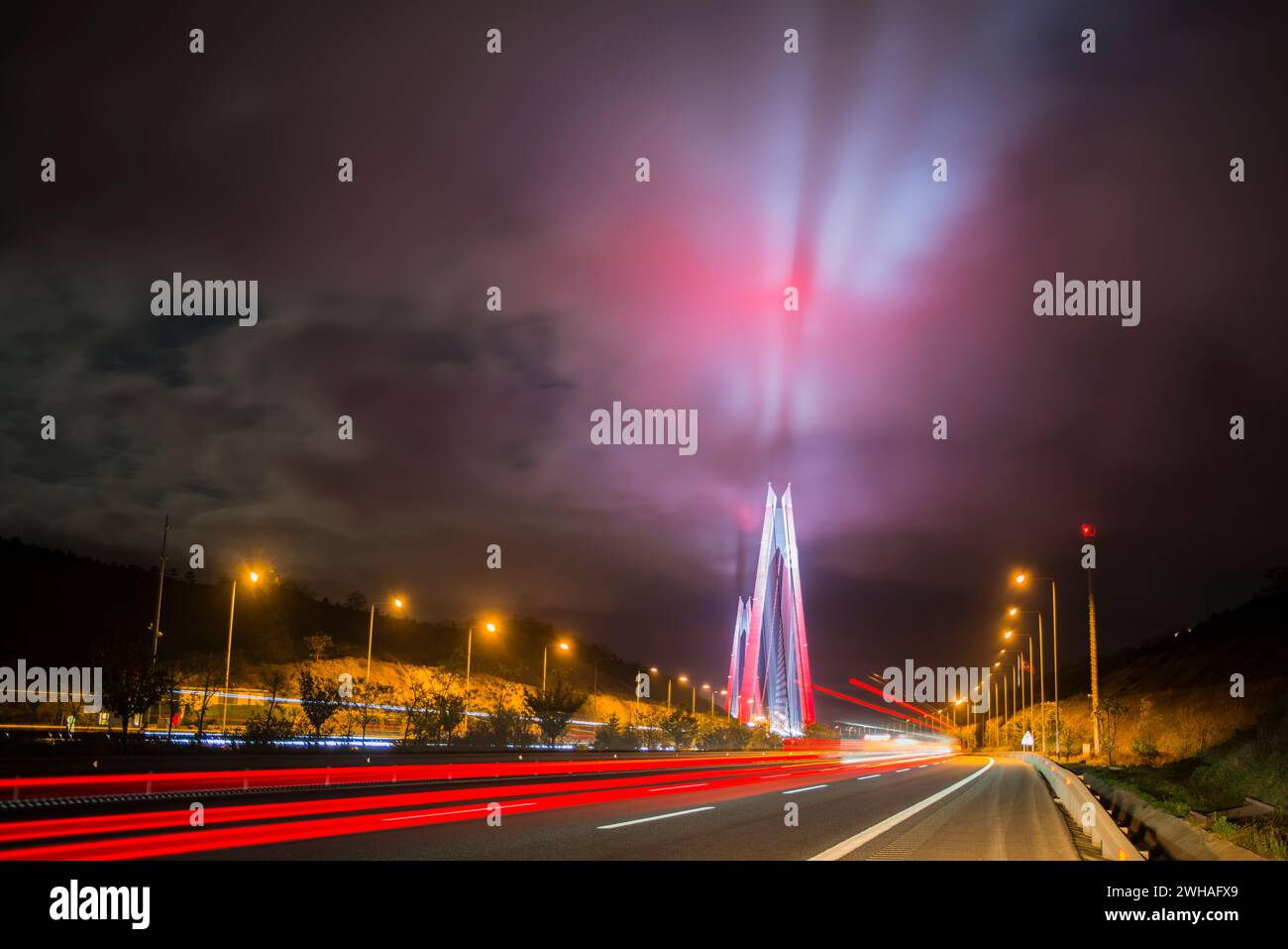 Il Ponte sul Bosforo di notte, adornato da vivaci luci rosse che si riflettono sulle nuvole, creando un paesaggio urbano drammatico e colorato sopra Istanbul Foto Stock