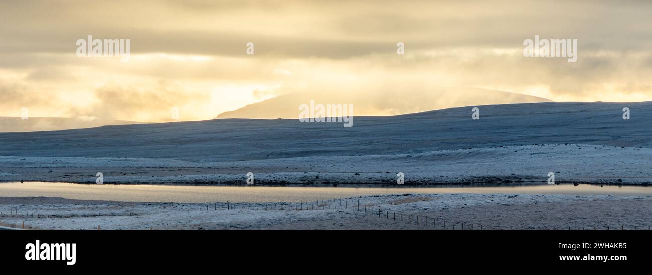 Spettacolare scenario della riva fredda del lago solitario in inverno sotto il cielo del tramonto durante le nevicate Foto Stock