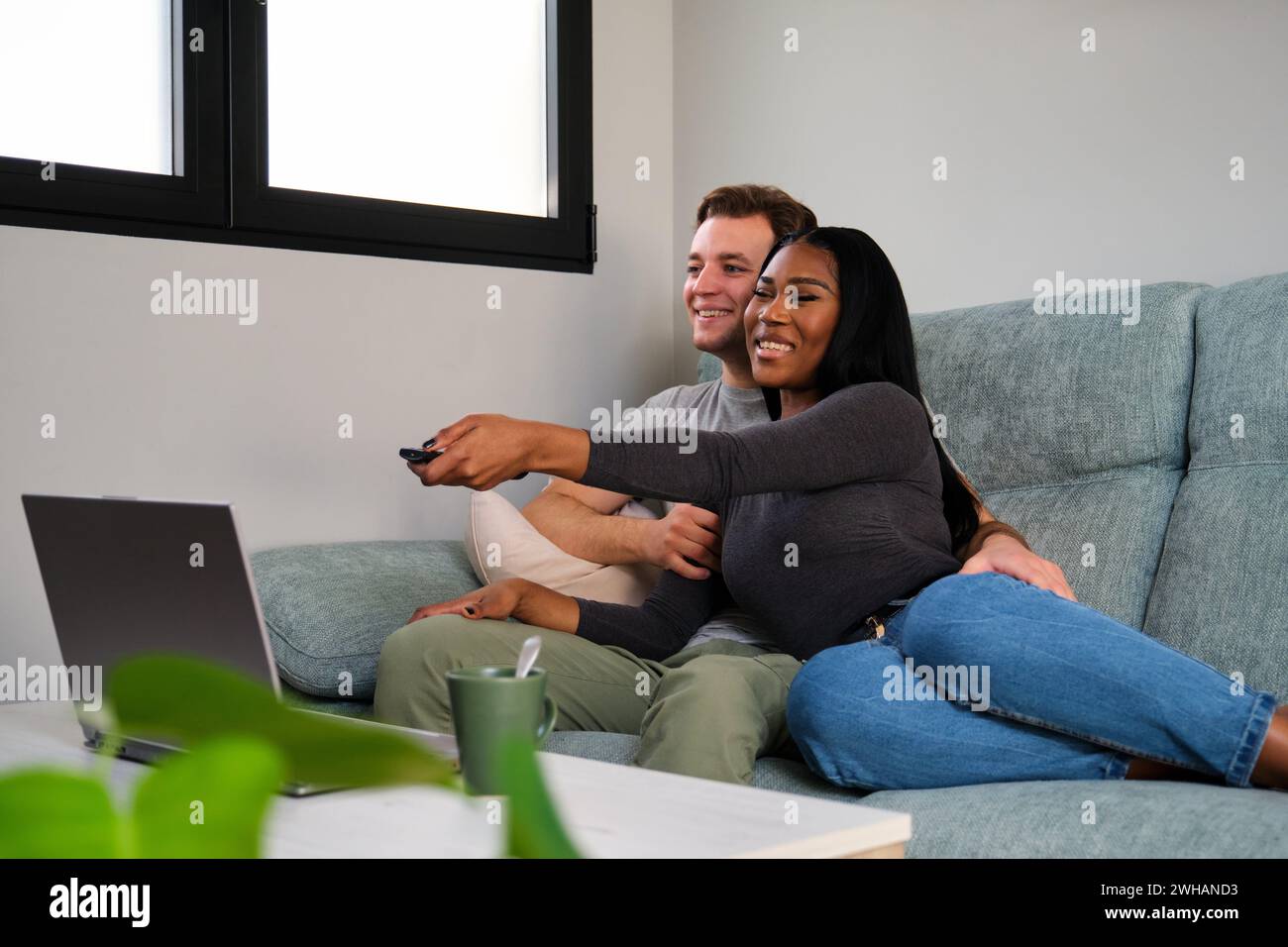 Coppia multietnica che guarda la TV seduto su un divano a casa. Foto Stock